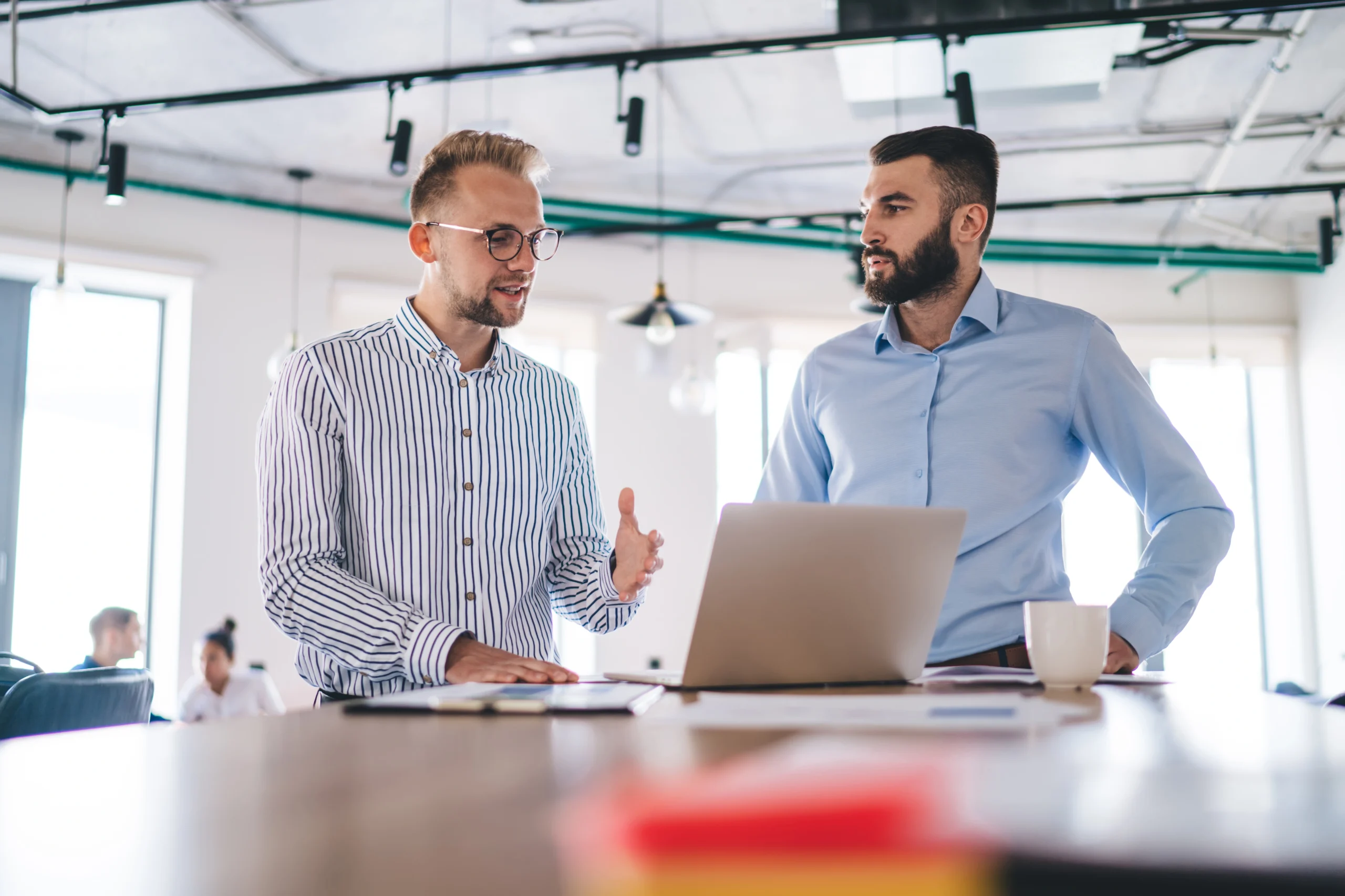 Two man standing in an office talking to each other in front of a laptop